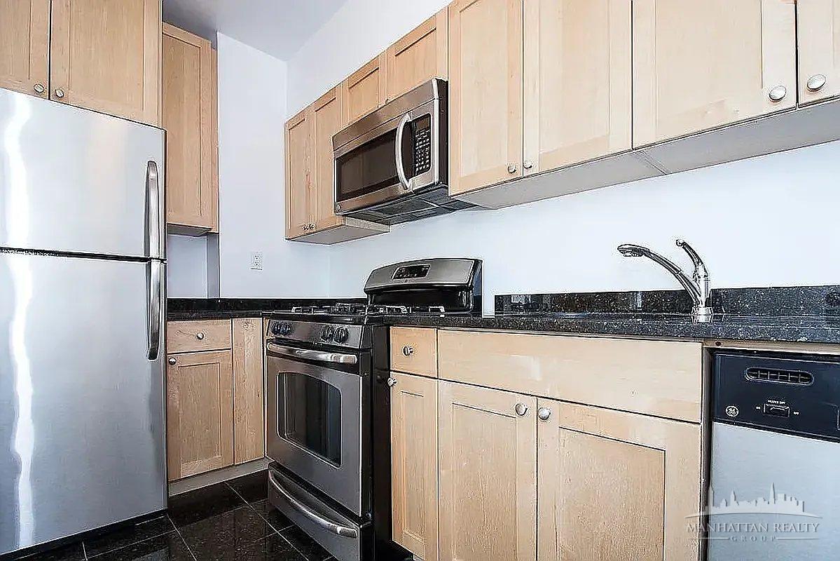 95 Christopher Street, Unit 4J Manhattan, NY 10014 - Photo 4 of 8 a kitchen with stainless steel appliances granite countertop white refrigerator stove a microwave oven and a sink with granite countertops