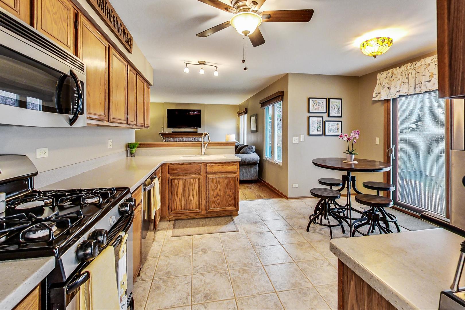 1174 Sweetwater Ridge Lake In The Hills, IL 60156 - Photo 9 of 44 a kitchen with stainless steel appliances a stove a sink dishwasher a dining table and chairs with wooden floor