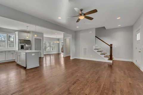 a view of an empty room with wooden floor and a kitchen
