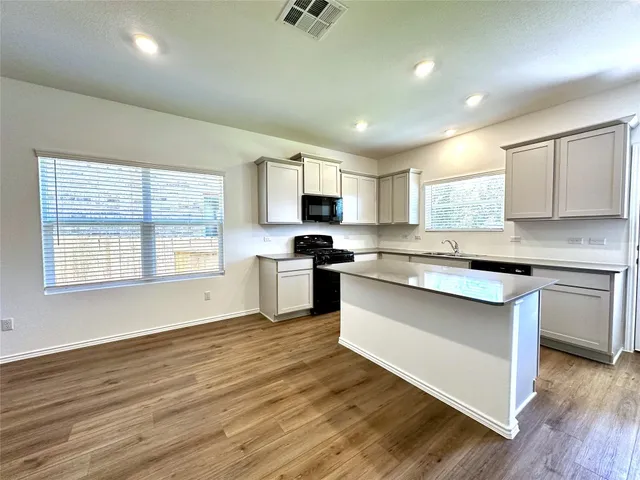 a kitchen with granite countertop wooden floors stainless steel appliances a sink and a window