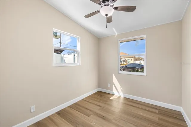 an empty room with wooden floor chandelier fan and windows