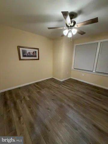 a view of an empty room with wooden floor and a ceiling fan