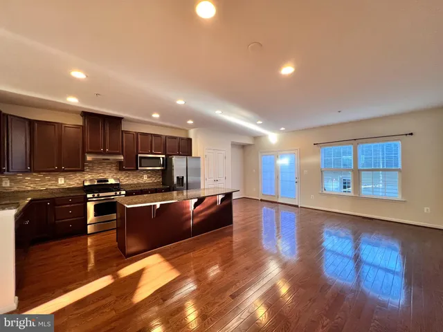 a large kitchen with stainless steel appliances granite countertop a large counter top a stove and a sink with wooden floor