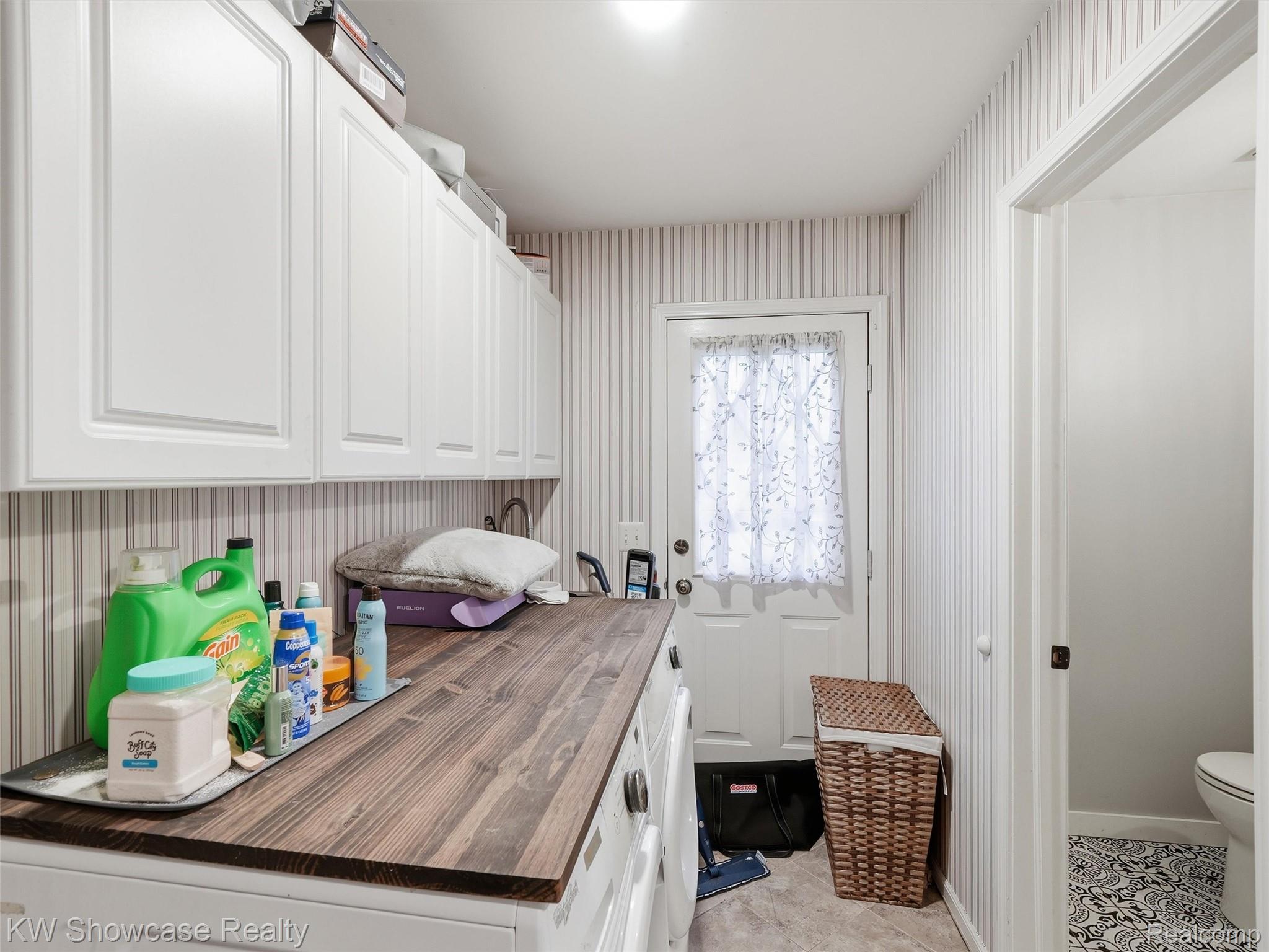 3360 Pleasant Valley Road Brighton, MI 48114 - Photo 28 of 60 Laundry room featuring extensive white shaker cabinetry, a wood-finish countertop, and a utility sink