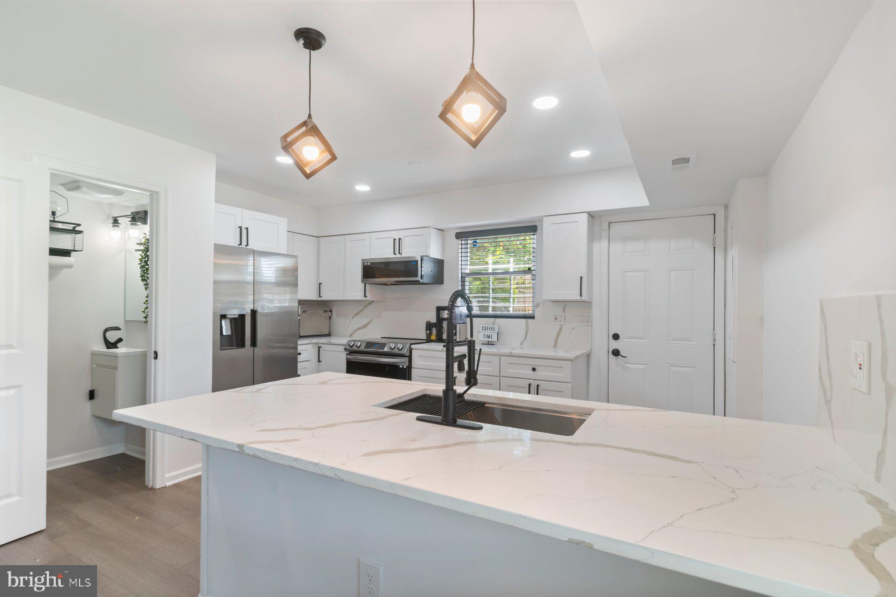 1221 East Oliver Street Baltimore, MD 21202 - Photo 6 of 26 a kitchen with stainless steel appliances kitchen island granite countertop a refrigerator a stove white cabinets and couches with wooden floor