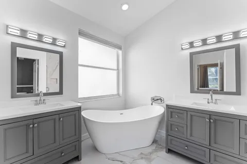 a bathroom with a double vanity sink a large mirror a bathtub and window