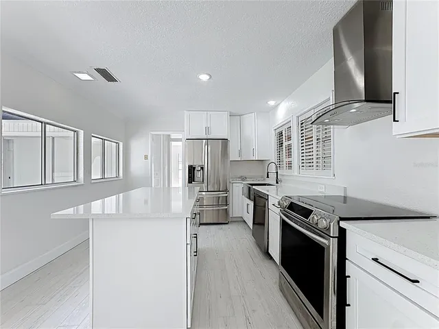 a view of kitchen with refrigerator stove and white cabinets with wooden floor