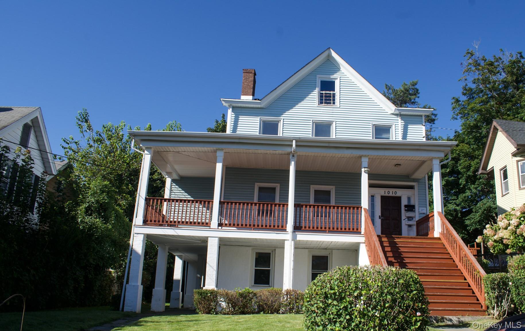 View of front of home featuring covered porch, a chimney, stairs, and a front lawn