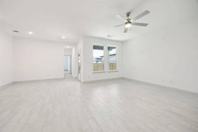 an empty room with chandelier fan and windows