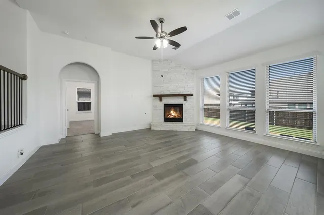 an empty room with wooden floor a ceiling fan and windows