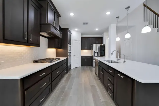 a large kitchen with a large counter top a sink stainless steel appliances and cabinets