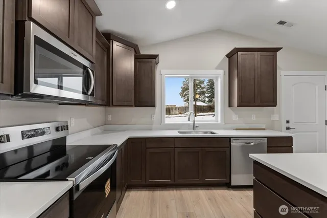 a large kitchen with stainless steel appliances a stove a sink a refrigerator a center island a wooden floor and a sink