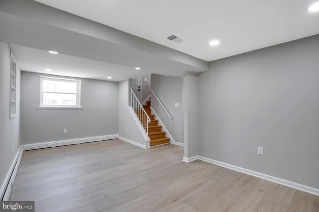 an empty room with wooden floor staircase and windows
