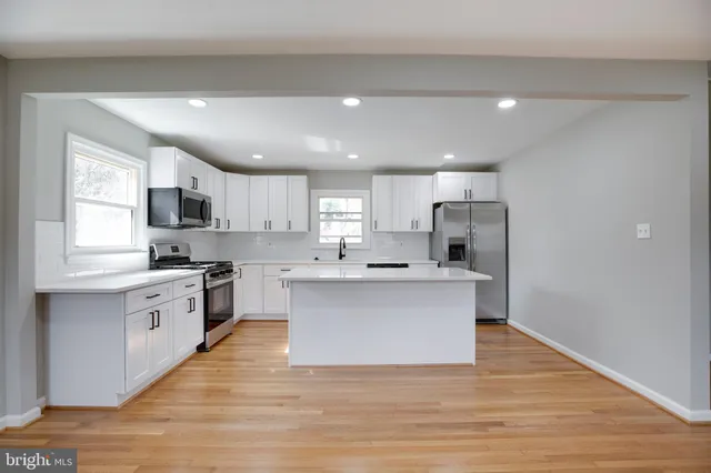 a large kitchen with stainless steel appliances granite countertop a stove top oven a sink dishwasher a refrigerator and white cabinets with wooden floor