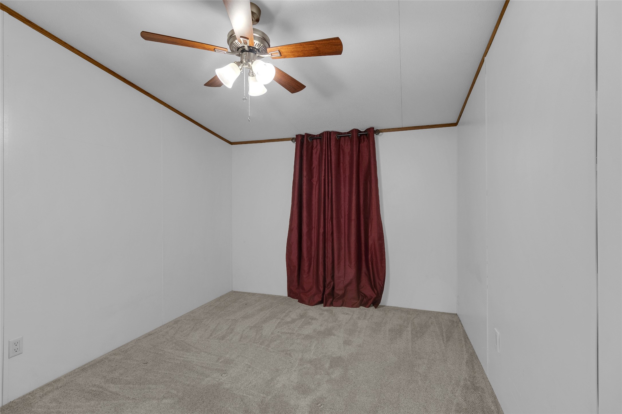22094 Spear Road Porter, TX 77365 - Photo 29 of 45 Third bedroom features neutral carpet and walls, accented by a ceiling fan with wooden blades. A window with dark red curtains. The space is simple and versatile, ideal for use as a bedroom or office.