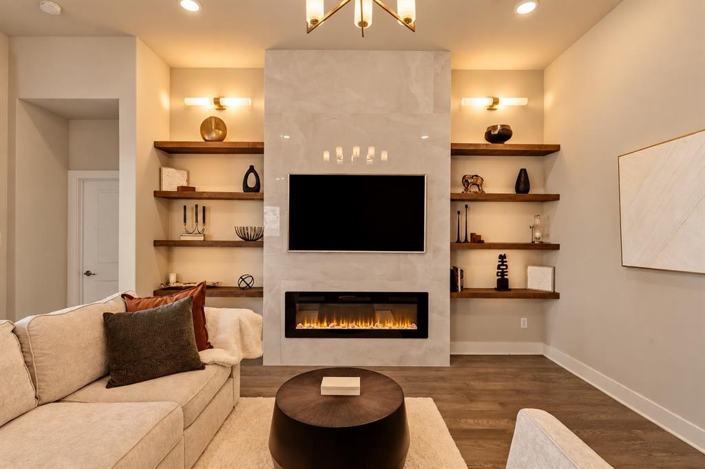 5112 Holy Springs Road Denton, TX 76207 - Photo 10 of 24 Inviting great room highlighted by custom lighting, rich built-in wood shelving, and a dramatic floor-to-ceiling porcelain-tiled electric fireplace offering both adjustable ambiance and heat. A concealed media box keeps a flush-mounted TV installation sleek and free of visible wires.