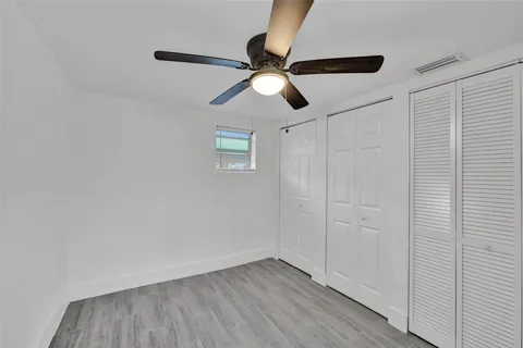 an empty room with wooden floor ceiling fan and window