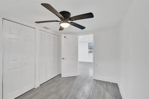 an empty room with wooden floor ceiling fan and window