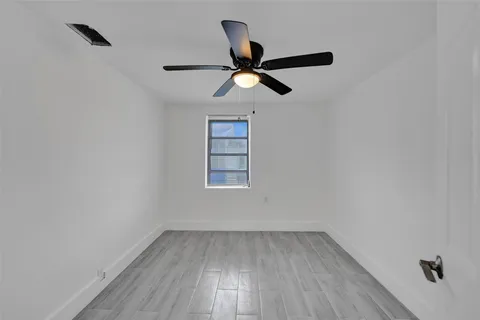 an empty room with wooden floor ceiling fan and window