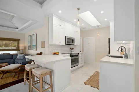 a kitchen with stainless steel appliances a stove a sink a refrigerator white cabinets and couches with wooden floor
