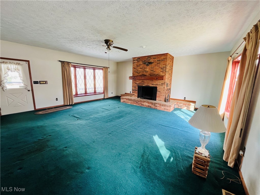 3210 Austinburg Road Ashtabula, OH 44004 - Photo 17 of 48 Unfurnished living room featuring ceiling fan, a textured ceiling, baseboards, a brick fireplace, and carpet
