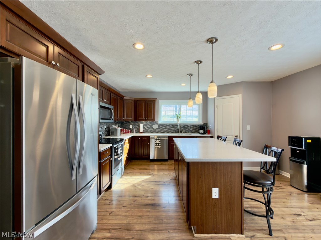 17377 Murphy Road Amesville, OH 45711 - Photo 13 of 43 Kitchen featuring stainless steel appliances, a breakfast bar, light wood-style floors, a kitchen island, and hanging light fixtures