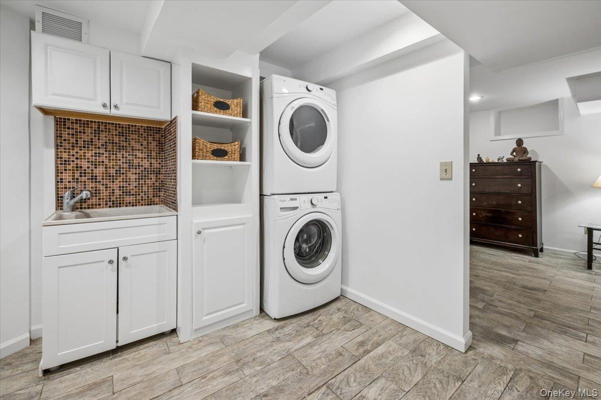 46 Bedford Road Katonah, NY 10536 - Photo 22 of 34 Dedicated laundry area featuring a stacked washer and dryer, white cabinetry with built-in shelving, a utility sink with a mosaic tile backsplash, and wood-finish flooring