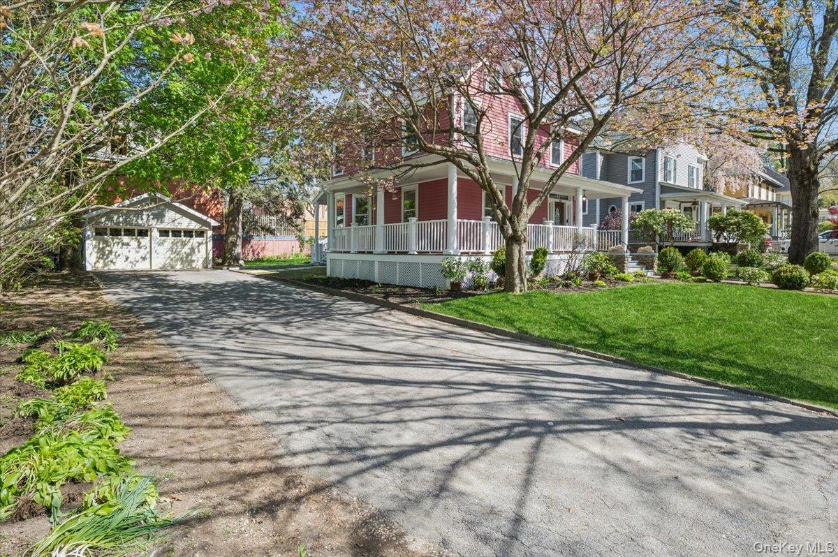 46 Bedford Road Katonah, NY 10536 - Photo 30 of 34 Crimson-hued residence featuring a white-railed porch, a verdant lawn, a detached two-car garage, and a paved driveway