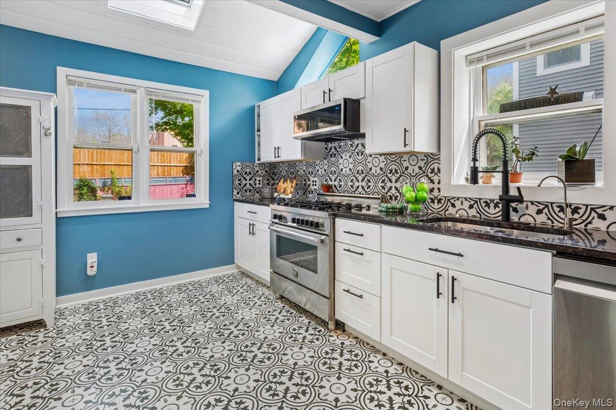 46 Bedford Road Katonah, NY 10536 - Photo 10 of 34 Kitchen featuring bold patterned floor tiles, white shaker cabinetry with dark hardware, stainless steel appliances, black countertops, and a decorative tile backsplash