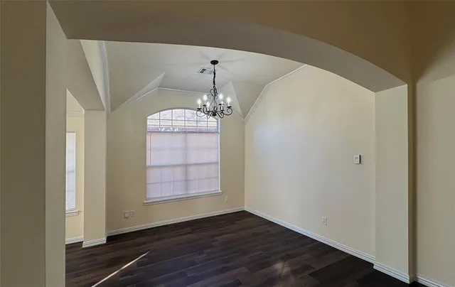 an empty room with wooden floor chandelier and windows