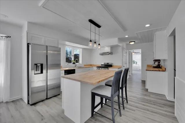 a kitchen with stainless steel appliances kitchen island granite countertop a refrigerator a stove a sink dishwasher and a dining table with wooden floor