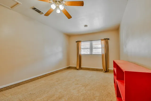 an empty room with chandelier fan and windows