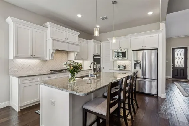 a kitchen with stainless steel appliances granite countertop a dining table chairs refrigerator and microwave