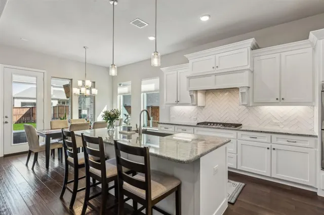 a kitchen with stainless steel appliances granite countertop a stove a sink a dining table and chairs with wooden floor