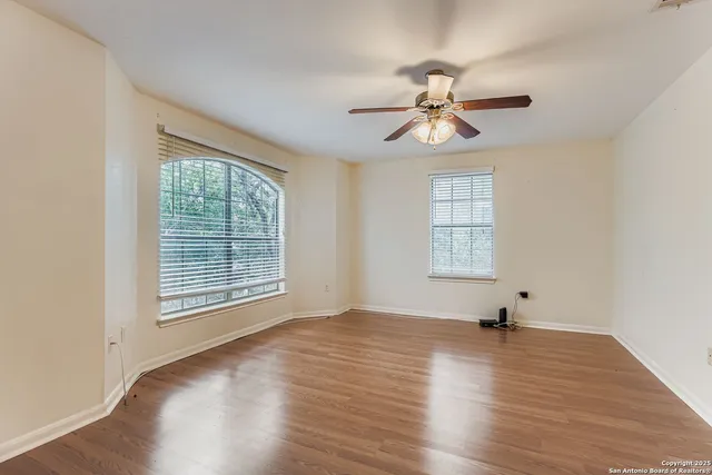 an empty room with wooden floor chandelier fan and windows