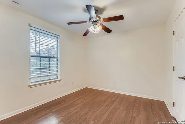an empty room with wooden floor ceiling fan and windows