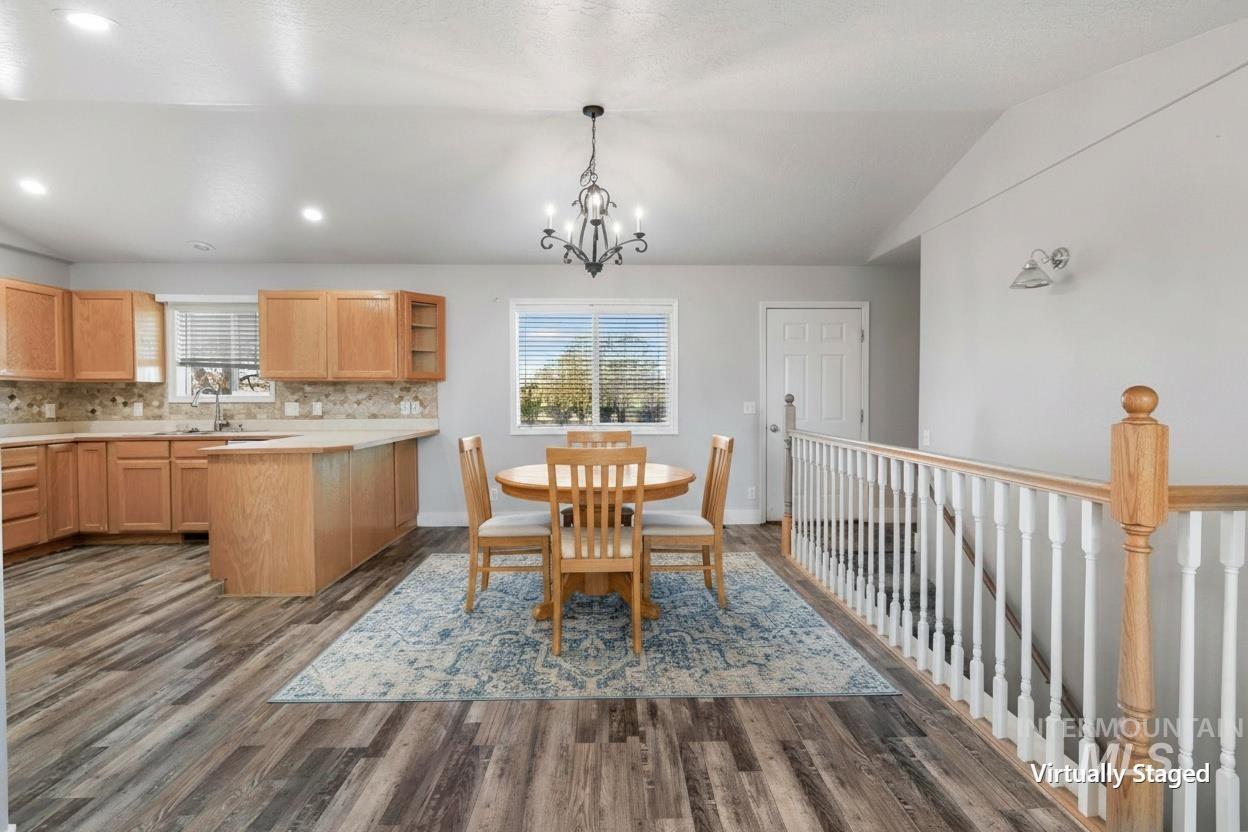 445 South College Street Oakley, ID 83346 - Photo 4 of 24 Open-concept living space with wood-finish flooring, a kitchen featuring wood cabinetry and a tile backsplash, and a dining area illuminated by a chandelier