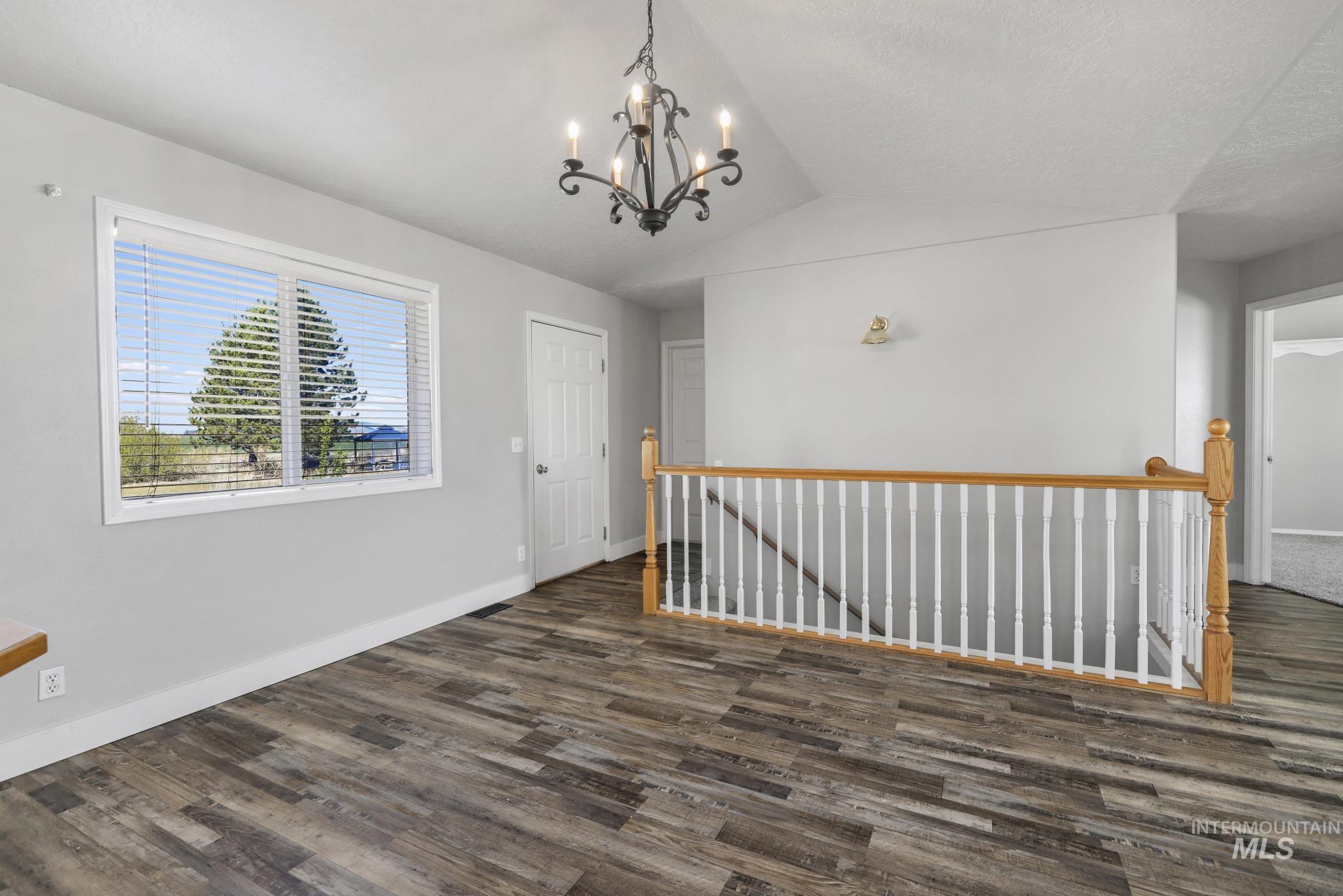 445 South College Street Oakley, ID 83346 - Photo 7 of 24 Empty room featuring lofted ceiling, dark wood-style flooring, and suspended lighting
