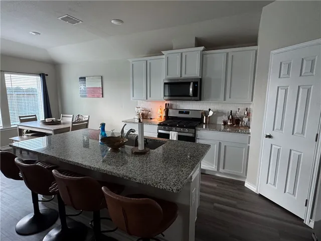 a kitchen with stainless steel appliances granite countertop a table chairs sink refrigerator and cabinets