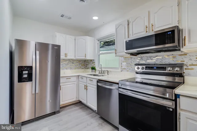 a kitchen with stainless steel appliances granite countertop a refrigerator oven a sink and white cabinets