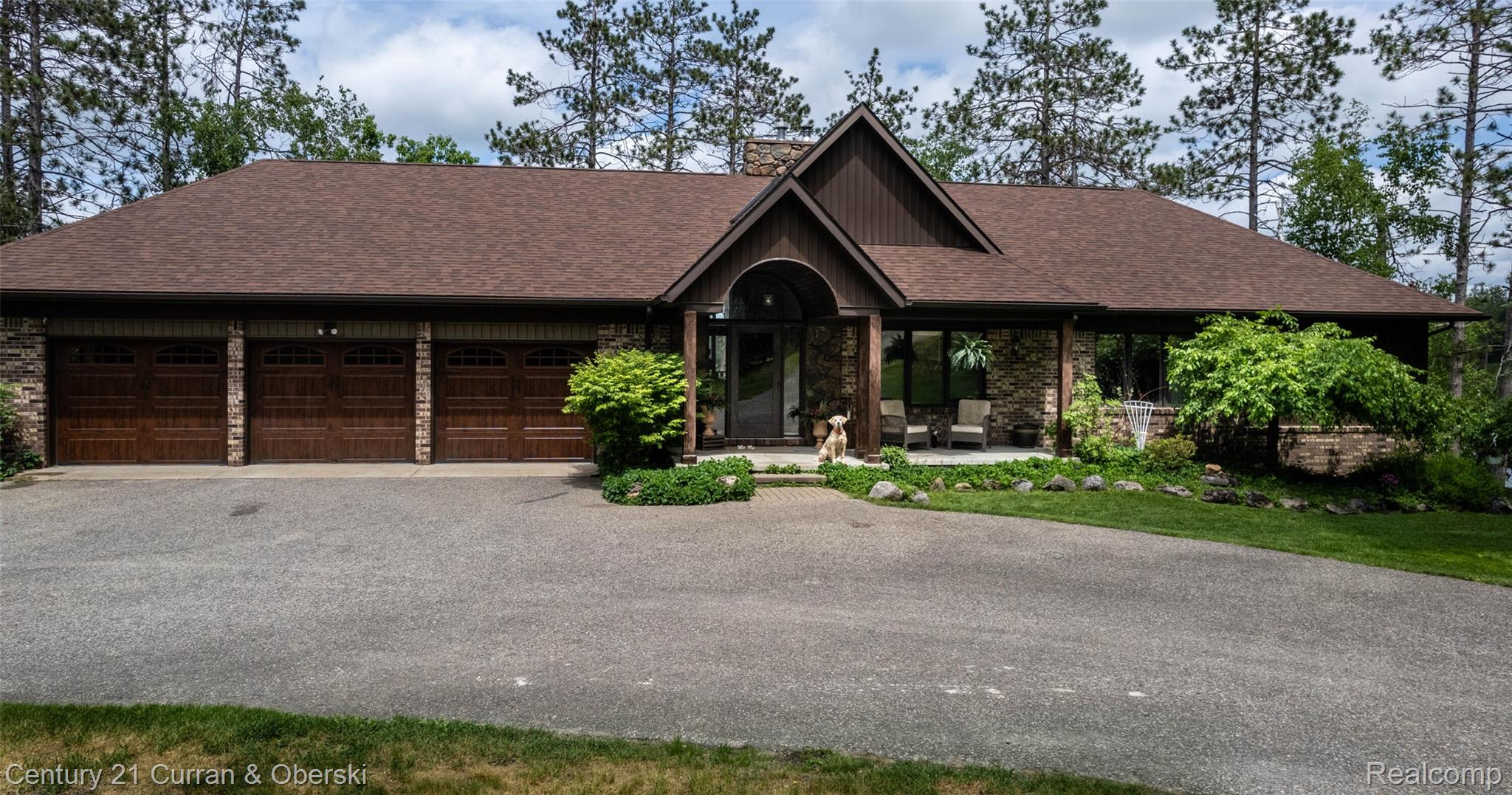 8775 Winding Rdg Drive Millersburg, MI 49759 - Photo 7 of 53 Stone and wood-sided exterior featuring a three-car garage with wood-finish doors, a prominent arched entry, and a paved driveway