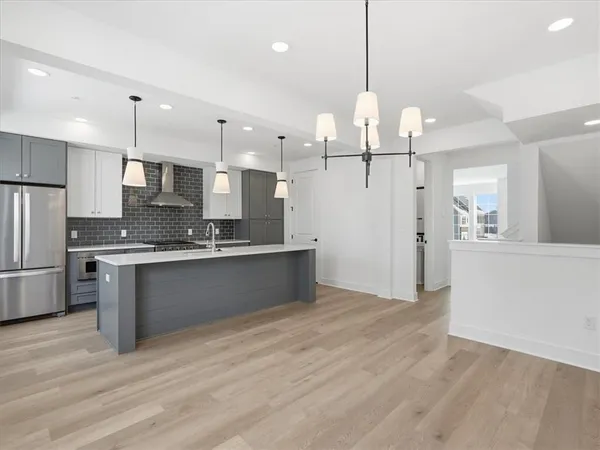 a large kitchen with granite countertop a large refrigerator a sink dishwasher a oven and white cabinets with wooden floor