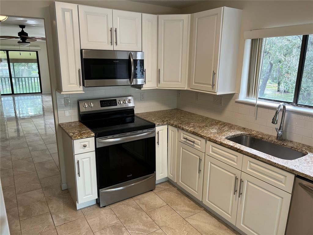 510 Mistletoe Court, Unit D Safety Harbor, FL 34695 - Photo 3 of 18 a kitchen with granite countertop white cabinets stainless steel appliances and a window