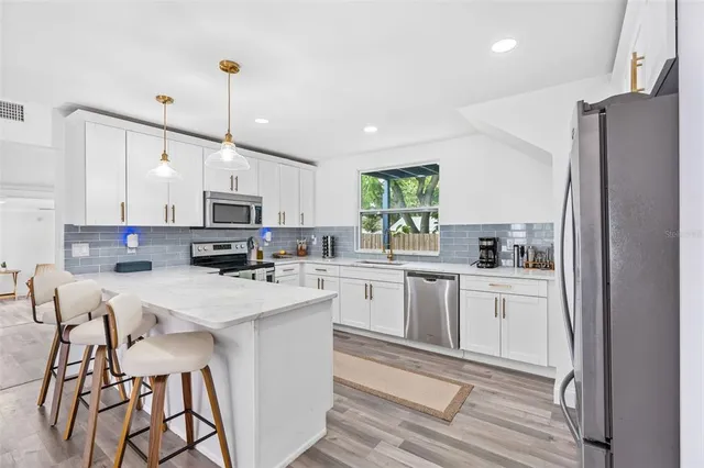 a kitchen with stainless steel appliances white cabinets a sink a stove a refrigerator and island