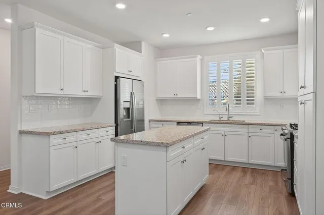 a kitchen with granite countertop a sink stove a refrigerator and white cabinets with wooden floor
