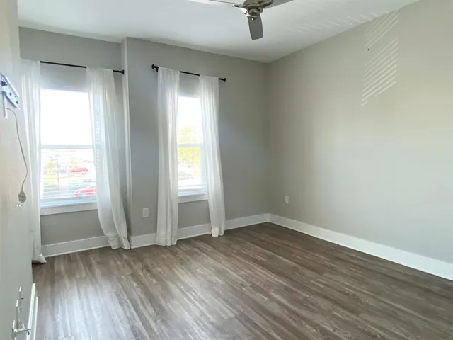 an empty room with wooden floor fan and windows