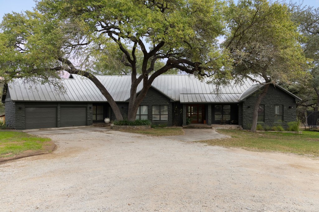 412 Rancho Grande Drive Wimberley, TX 78676 - Photo 3 of 37 View of front of property featuring a standing seam roof, dirt driveway, a metal roof, and an attached garage