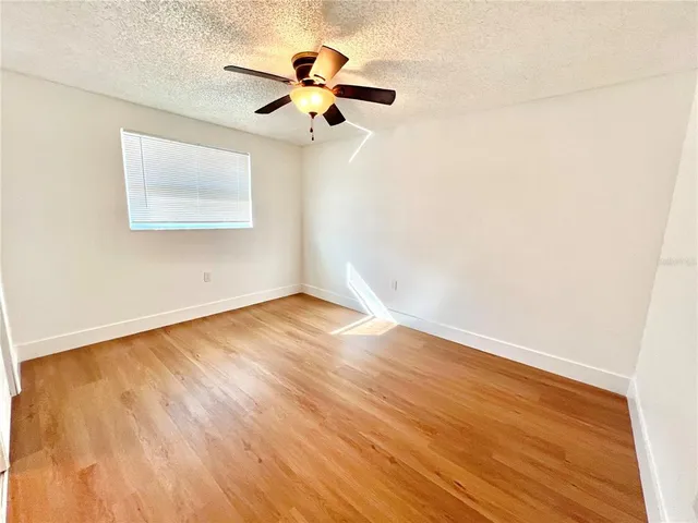an empty room with wooden floor fan and windows