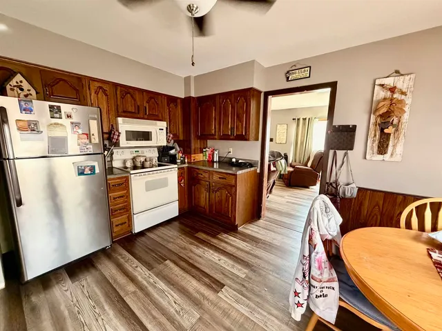a kitchen with stainless steel appliances granite countertop a refrigerator a sink dishwasher a stove a dining table and chairs with wooden floor