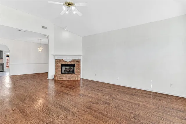 an empty room with wooden floor fireplace and windows